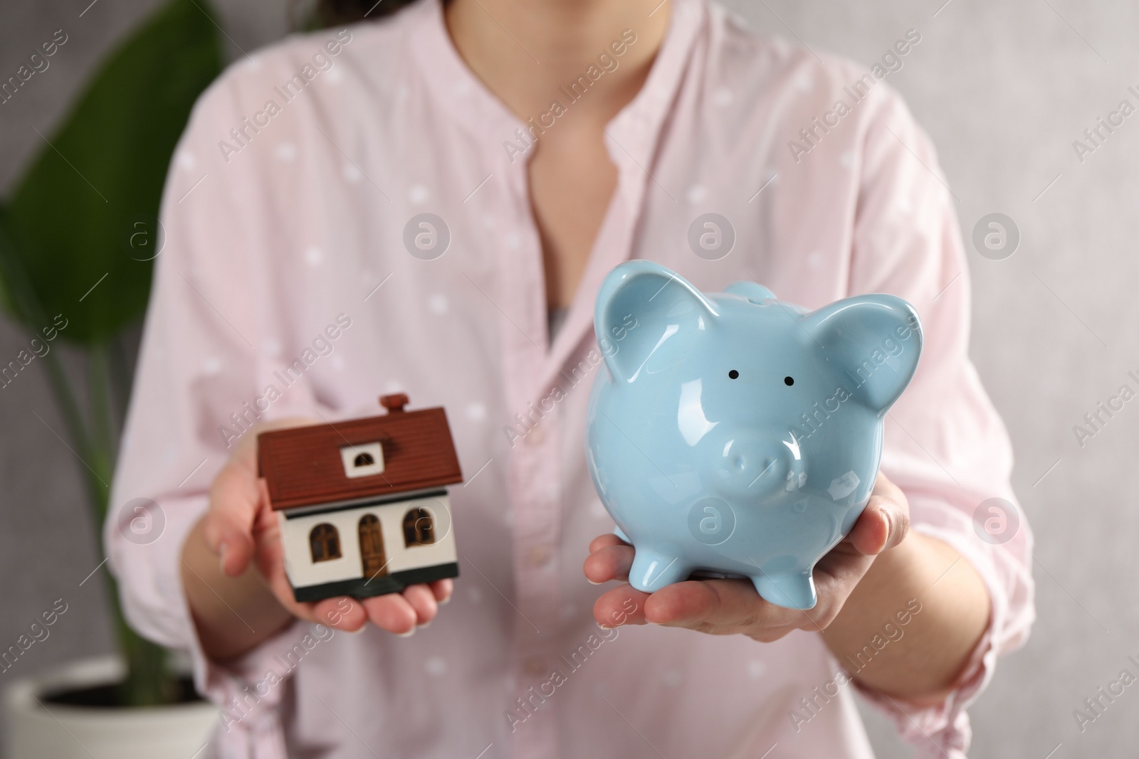 Photo of Woman with house model and piggy bank indoors, selective focus