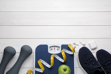 Flat lay composition with bathroom scale and measuring tape on white wooden floor, space for text. Weight loss concept