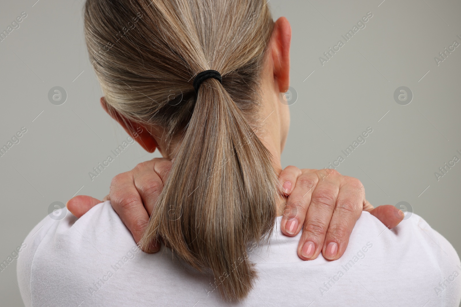 Photo of Mature woman suffering from pain in her neck on grey background, back view