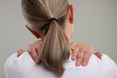 Mature woman suffering from pain in her neck on grey background, back view