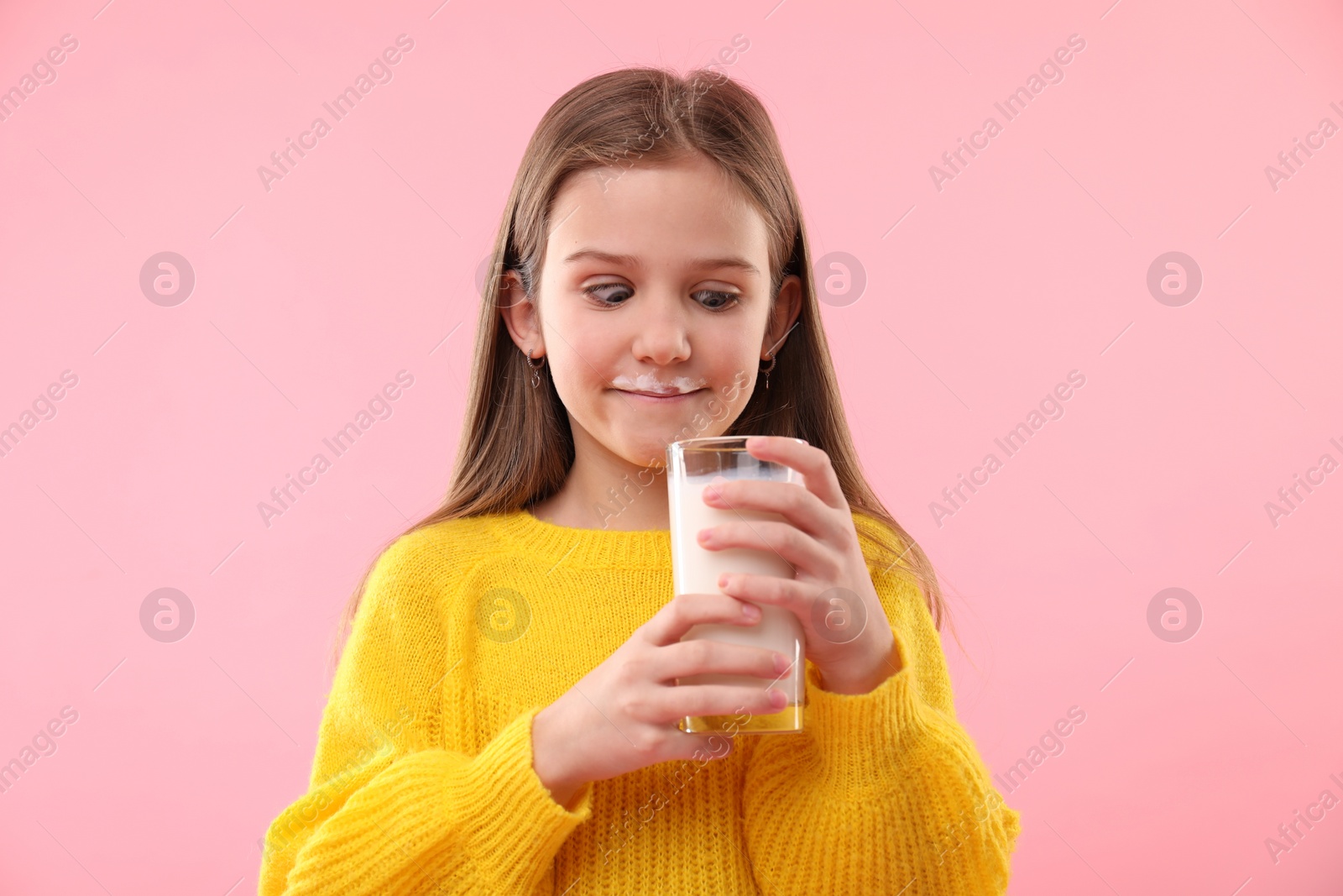 Photo of Funny little girl with milk mustache holding glass of tasty dairy drink on pink background