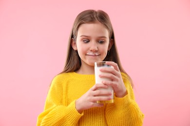 Photo of Funny little girl with milk mustache holding glass of tasty dairy drink on pink background
