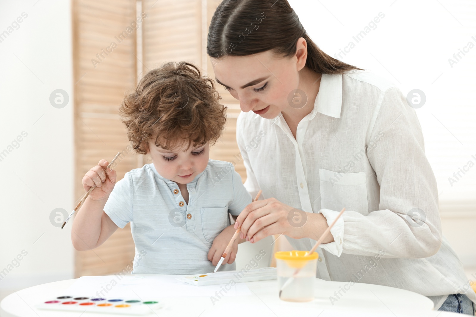 Photo of Mother and her little son painting with watercolor at home