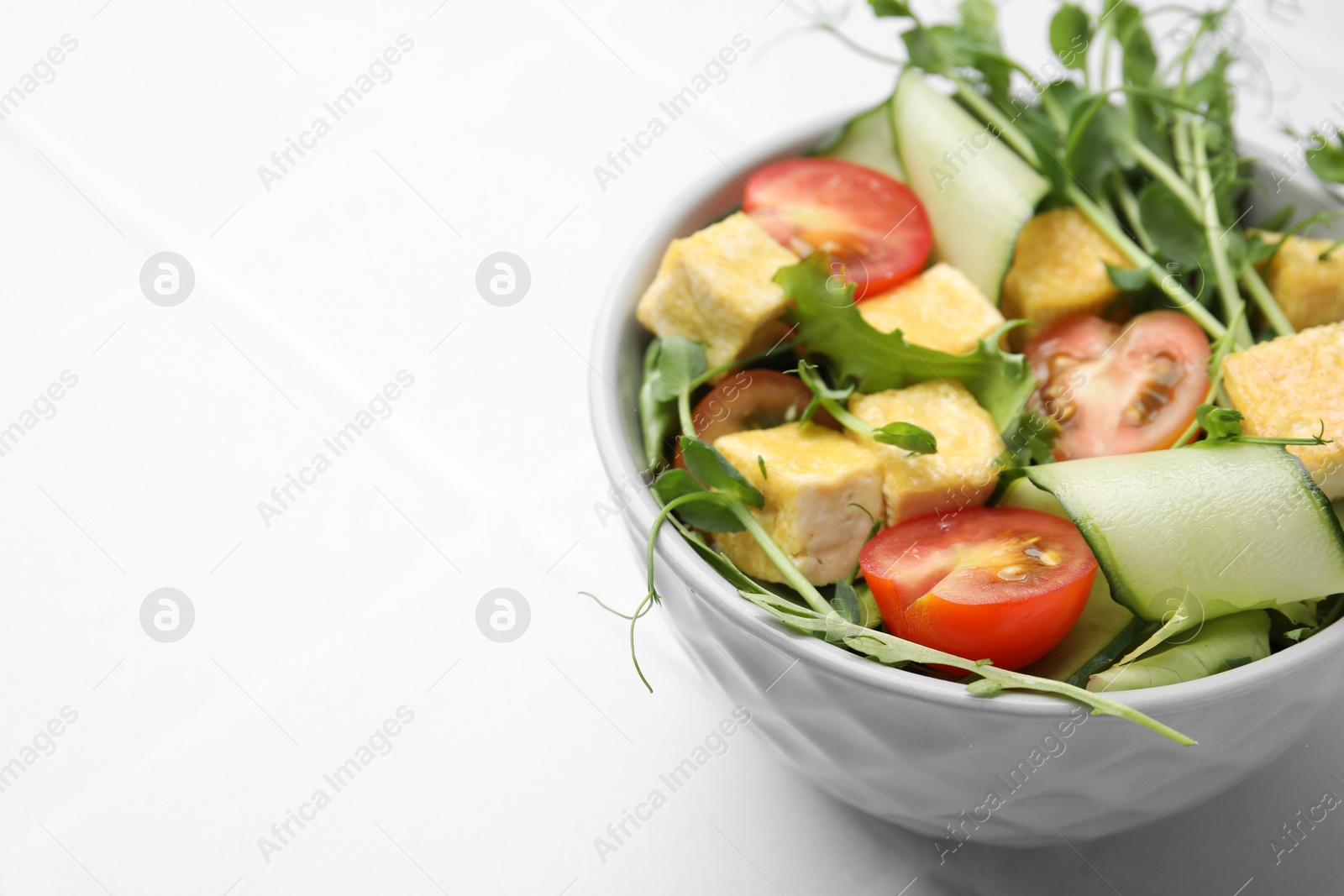 Photo of Bowl of tasty salad with tofu and vegetables on white tiled table, closeup. Space for text