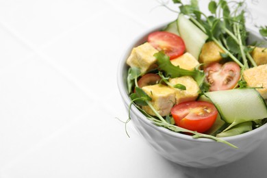 Bowl of tasty salad with tofu and vegetables on white tiled table, closeup. Space for text