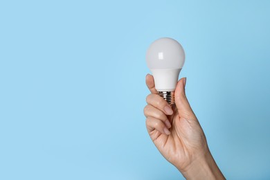 Photo of Woman holding LED light bulb on blue background, closeup. Space for text