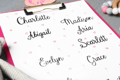 Photo of Clipboard with different baby names and toys on grey table, closeup