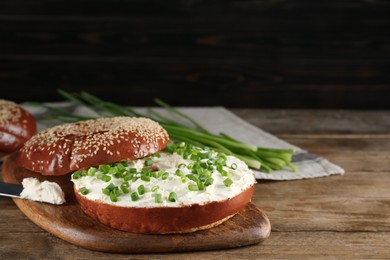 Delicious bagel with cream cheese and green onion on wooden table