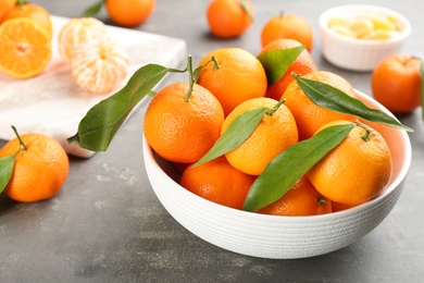 Photo of Fresh tangerines with green leaves on grey table, closeup