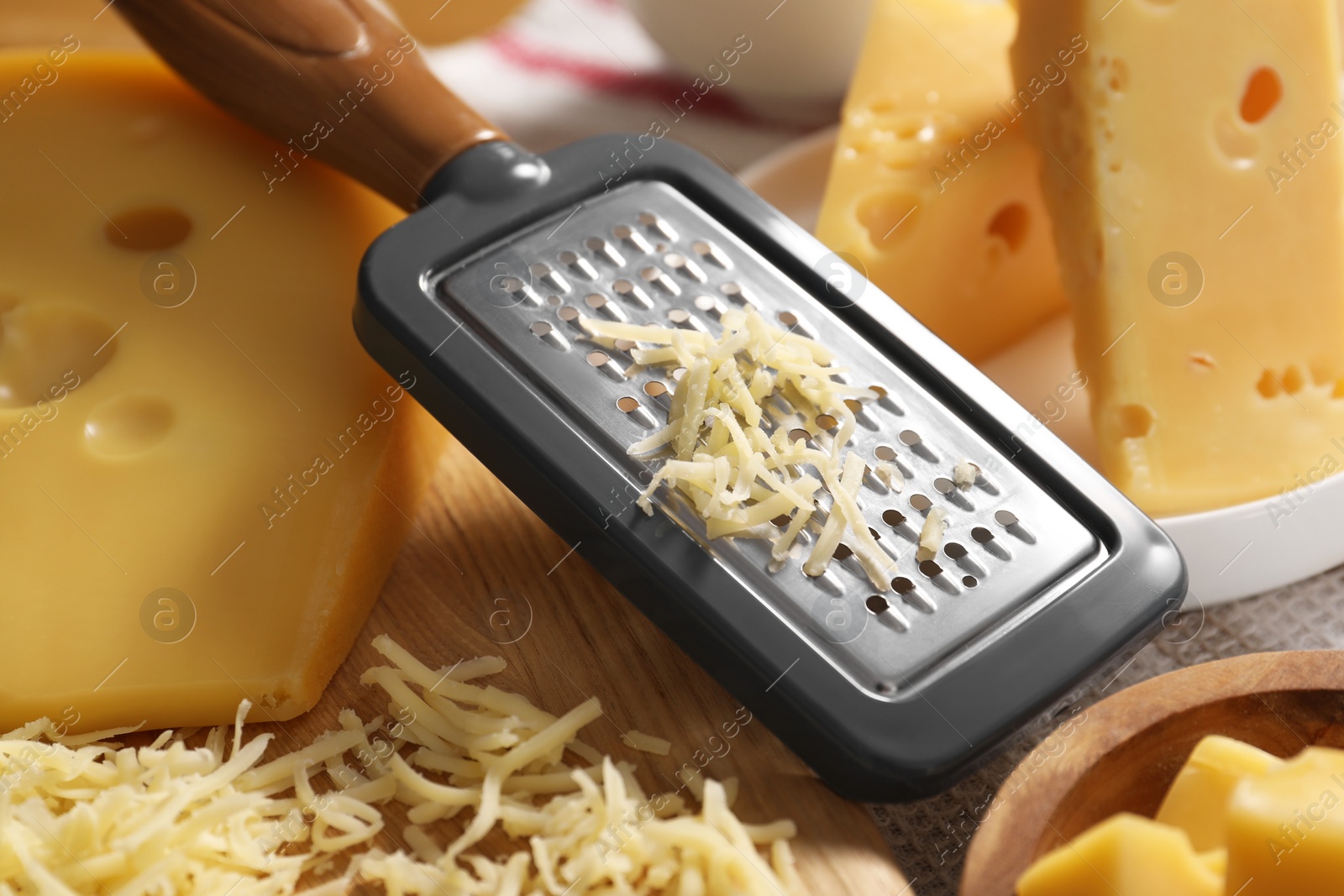 Photo of Grated, cut cheese and grater on table, closeup