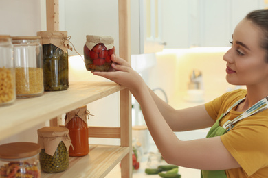 Photo of Woman putting jar of pickled vegetables on shelf indoors