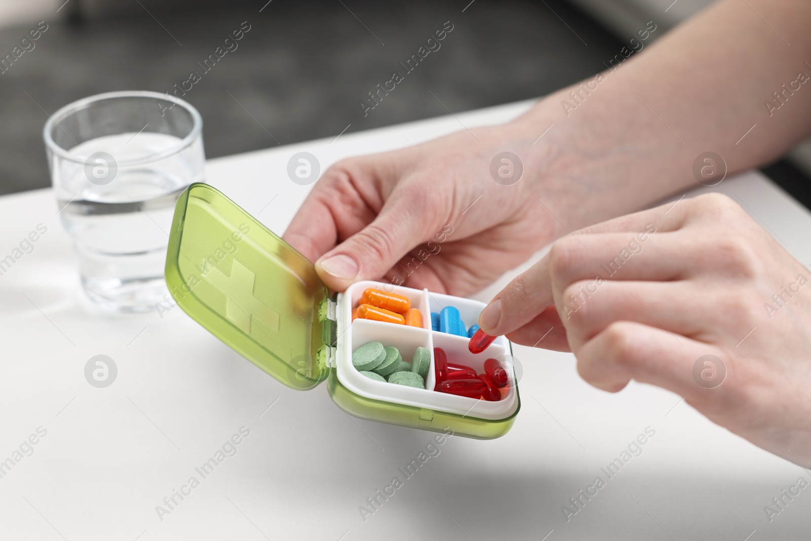 Photo of Woman with pills, organizer and glass of water at white table, closeup