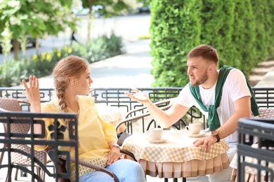 Photo of Young couple arguing while sitting in cafe, outdoors. Problems in relationship