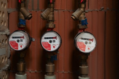 View of many electric meters near red brick wall. Water measuring device