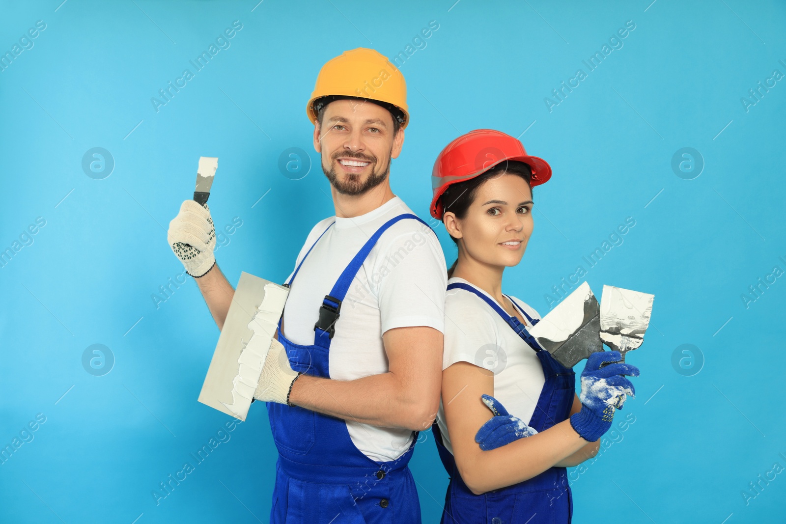 Photo of Professional workers with putty knives in hard hats on light blue background