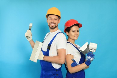 Photo of Professional workers with putty knives in hard hats on light blue background