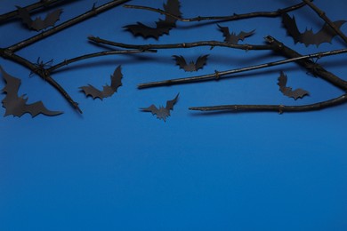 Black branches, paper bats and spiders on blue background, above view with space for text. Halloween celebration