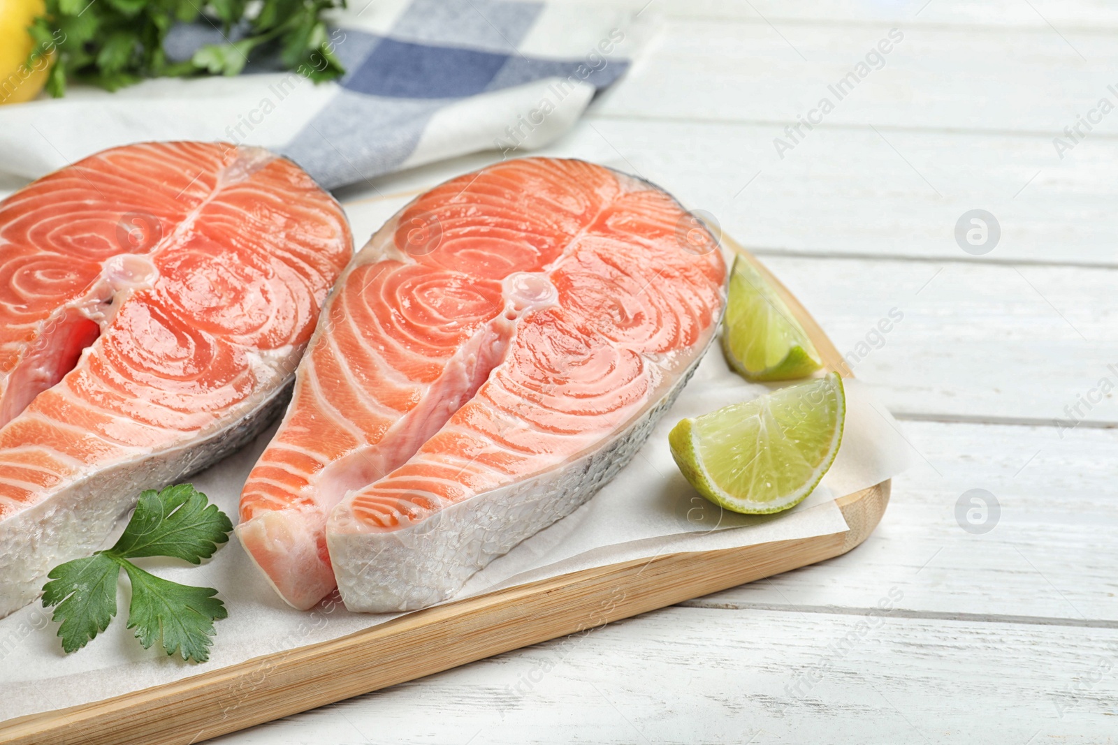 Photo of Fresh raw salmon with parsley and lime on white wooden table. Fish delicacy