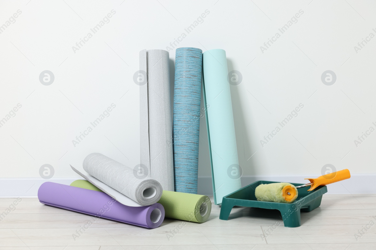 Photo of Different wallpaper rolls, roller and tray near white wall indoors