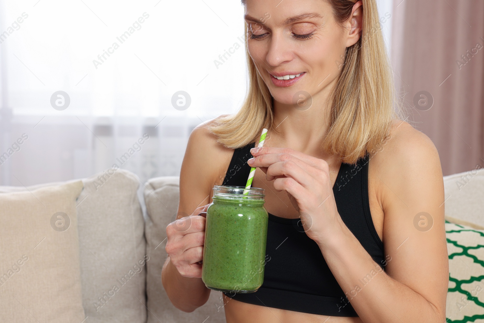 Photo of Young woman in sportswear with glass mason jar of fresh smoothie at home, closeup. Space for text