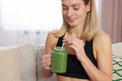 Young woman in sportswear with glass mason jar of fresh smoothie at home, closeup. Space for text