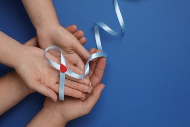 People holding light blue ribbon with paper blood drop on color background, top view and space for text. Diabetes awareness