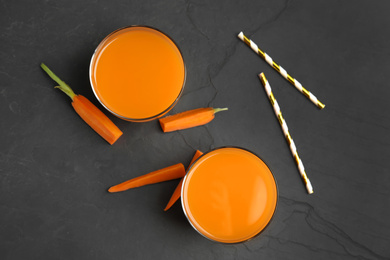 Photo of Glasses of freshly made carrot juice on black table, flat lay
