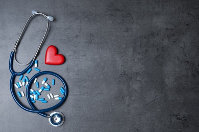 Flat lay composition with stethoscope, heart and pills on grey background, space for text. Cardiology concept