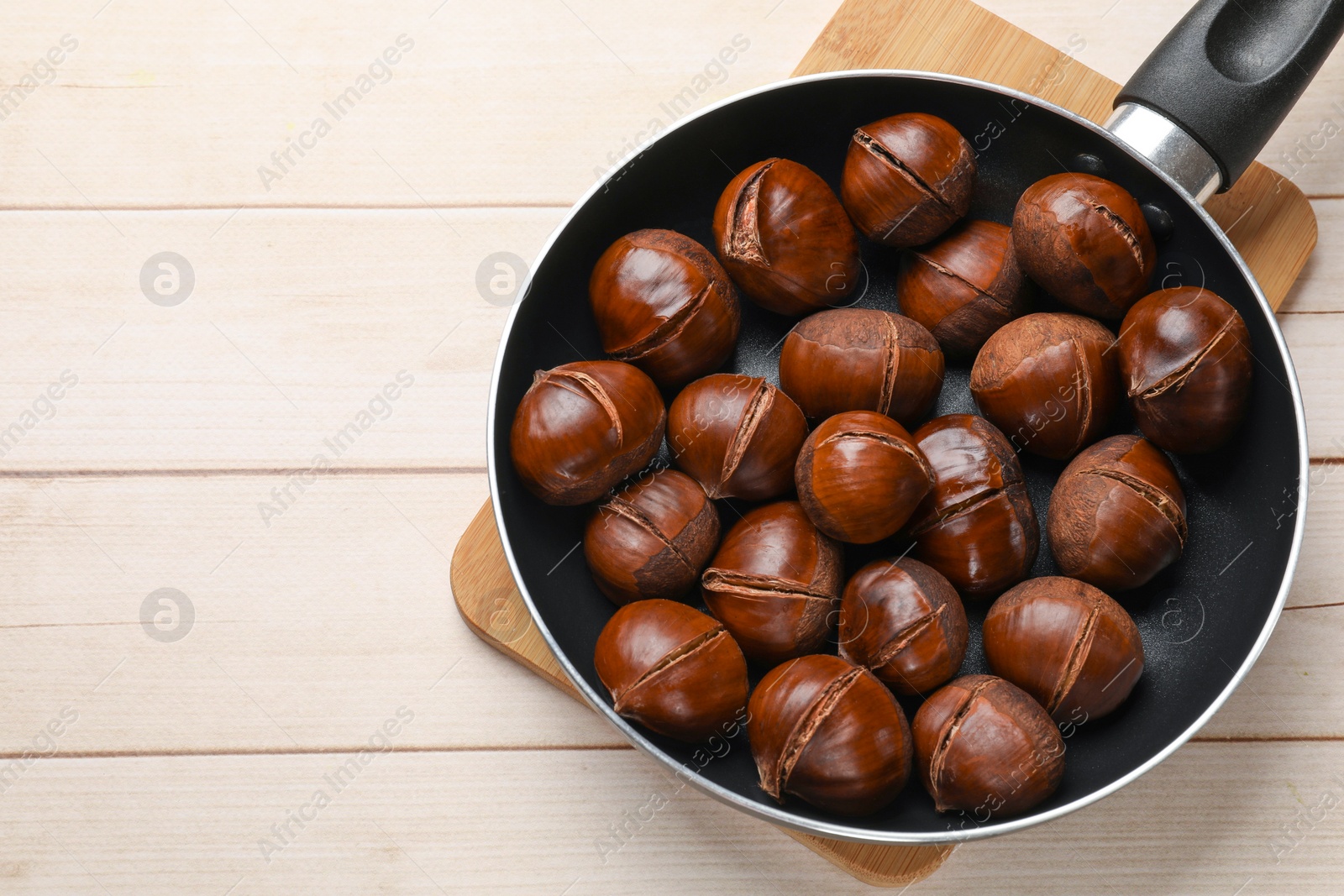 Photo of Roasted edible sweet chestnuts in frying pan on wooden table, top view. Space for text