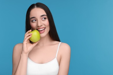 Beautiful young woman with apple on light blue background. Space for text