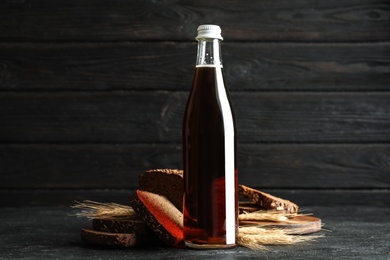 Photo of Bottle of delicious fresh kvass, spikelets and bread on grey table