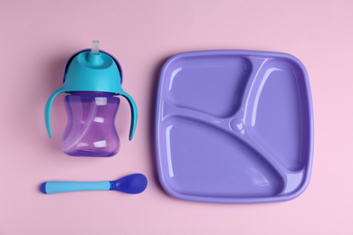 Set of colorful plastic dishware on light pink background, flat lay. Serving baby food