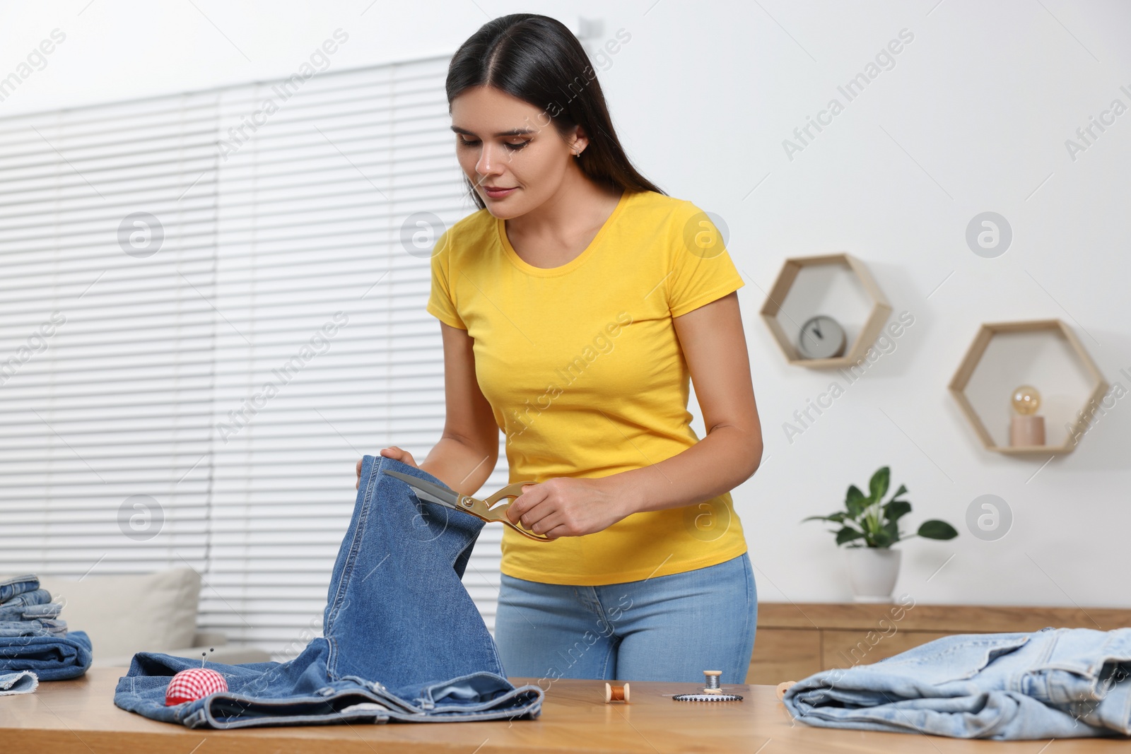 Photo of Young woman cutting jeans with scissors at wooden table indoors