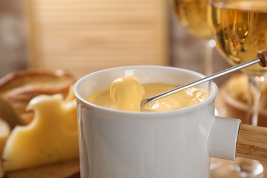 Pot of tasty cheese fondue and fork with bread on table