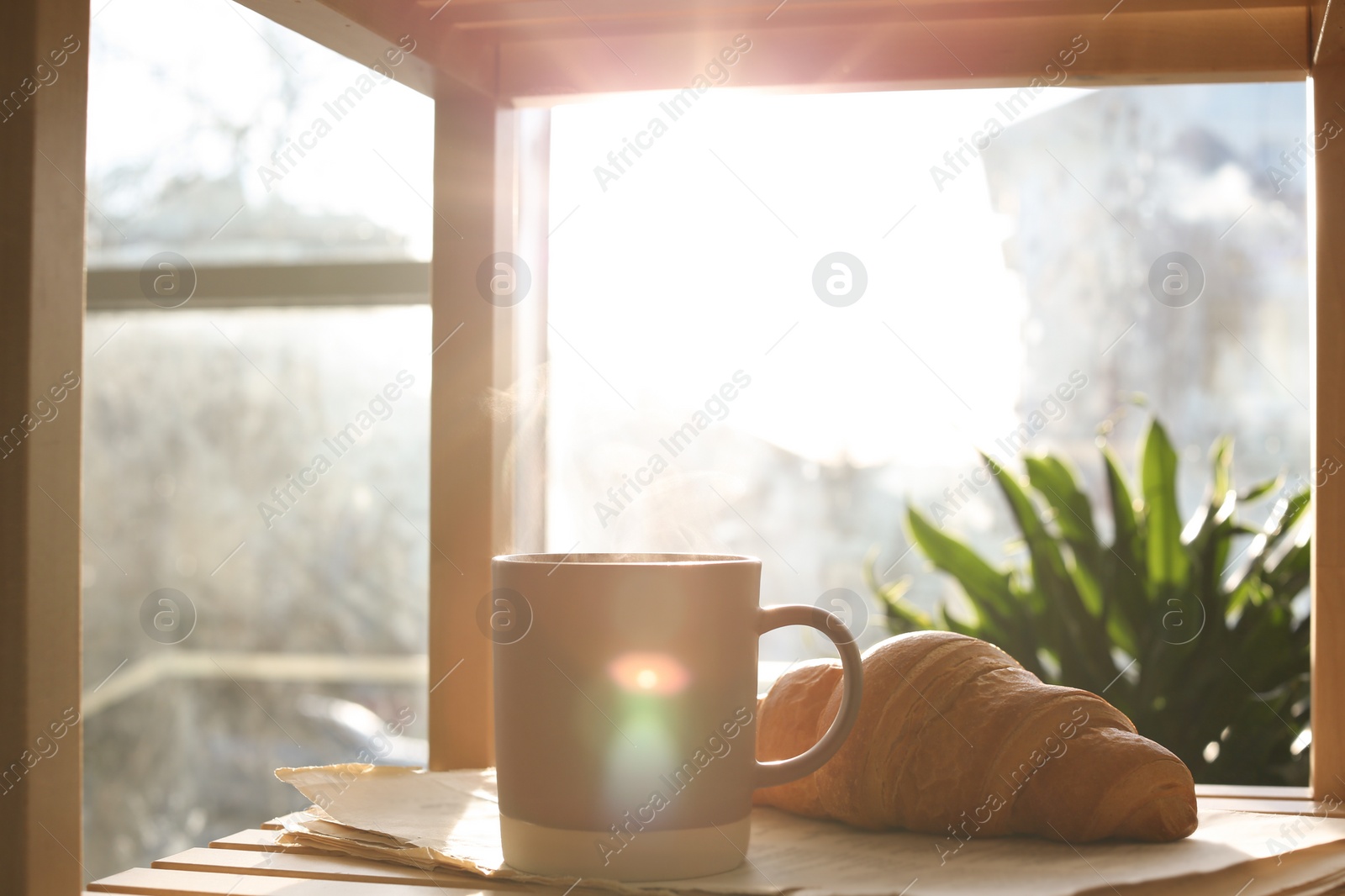 Photo of Delicious morning coffee, newspaper and croissant near window indoors
