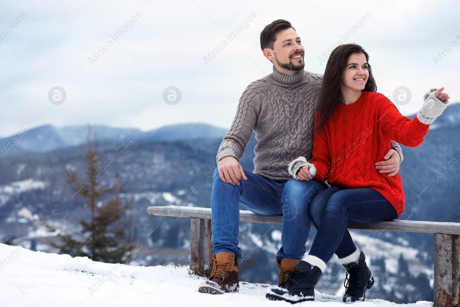 Photo of Couple sitting on bench in mountains, space for text. Winter vacation