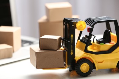 Photo of Toy forklift with boxes near laptop on table. Logistics and wholesale concept