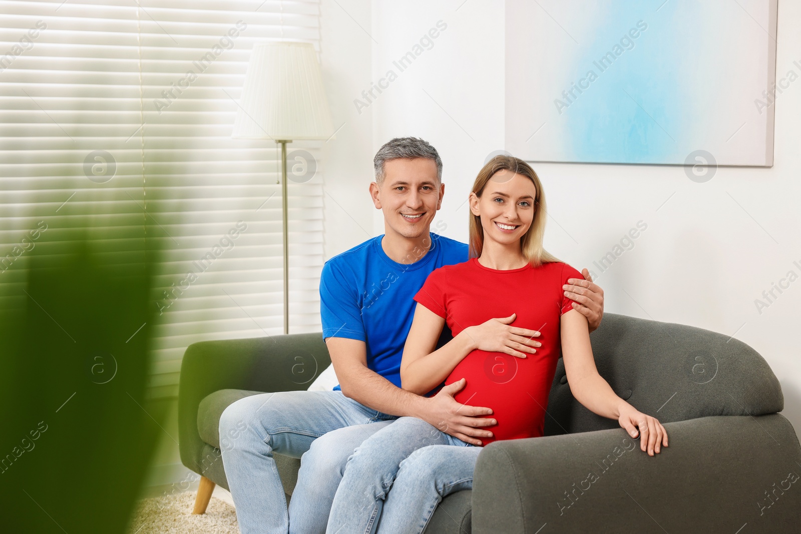 Photo of Young family housing concept. Pregnant woman with her husband on sofa at home