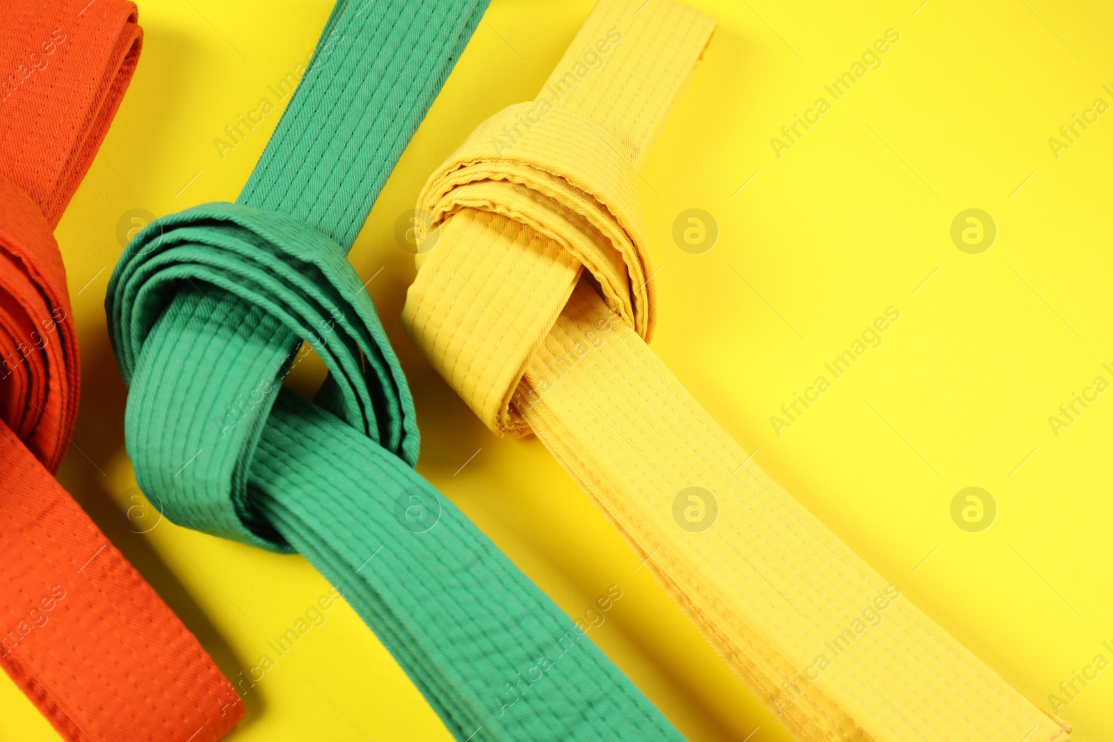 Photo of Colorful karate belts on yellow background, flat lay