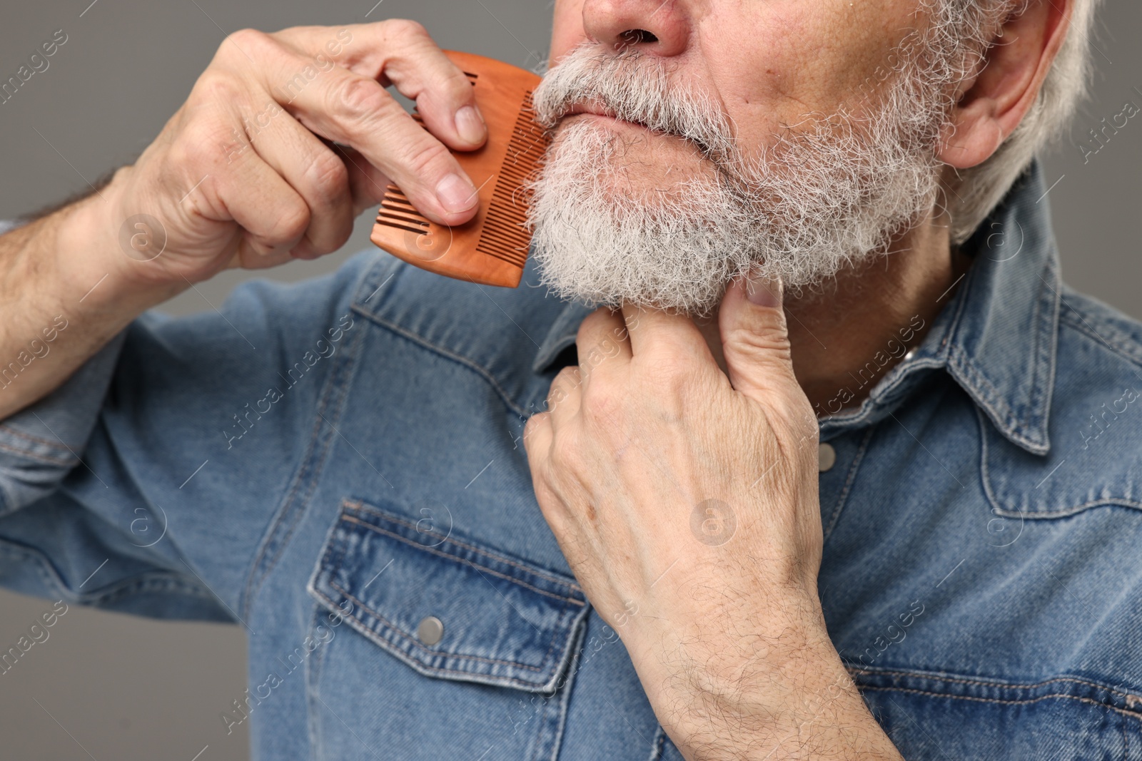 Photo of Man combing beard on grey background, closeup