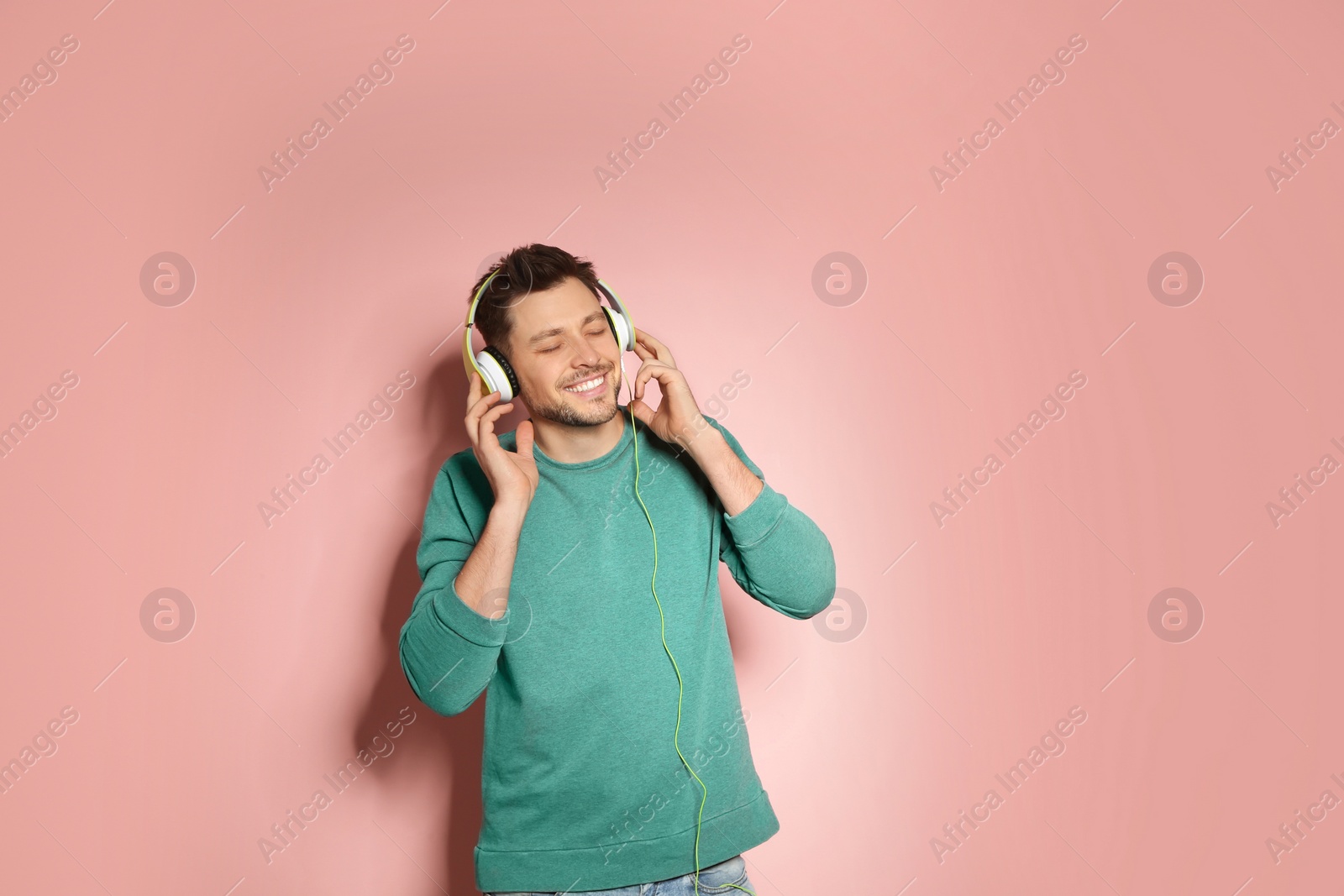 Photo of Handsome man listening to music with headphones on color background