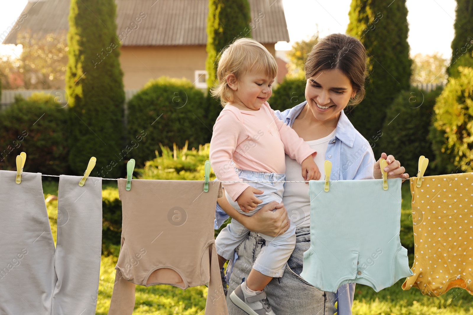 Photo of Mother and daughter hanging clothes with clothespins on washing line for drying in backyard