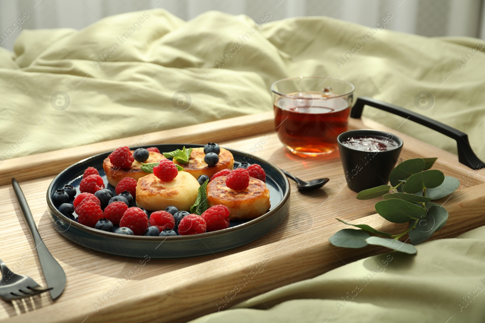 Photo of Tasty breakfast served in bedroom. Cottage cheese pancakes with fresh berries and mint on wooden tray