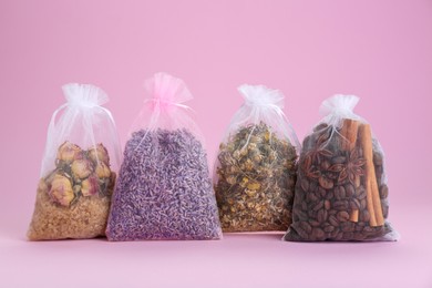 Photo of Scented sachets with dried flowers, coffee beans and spices on pink background