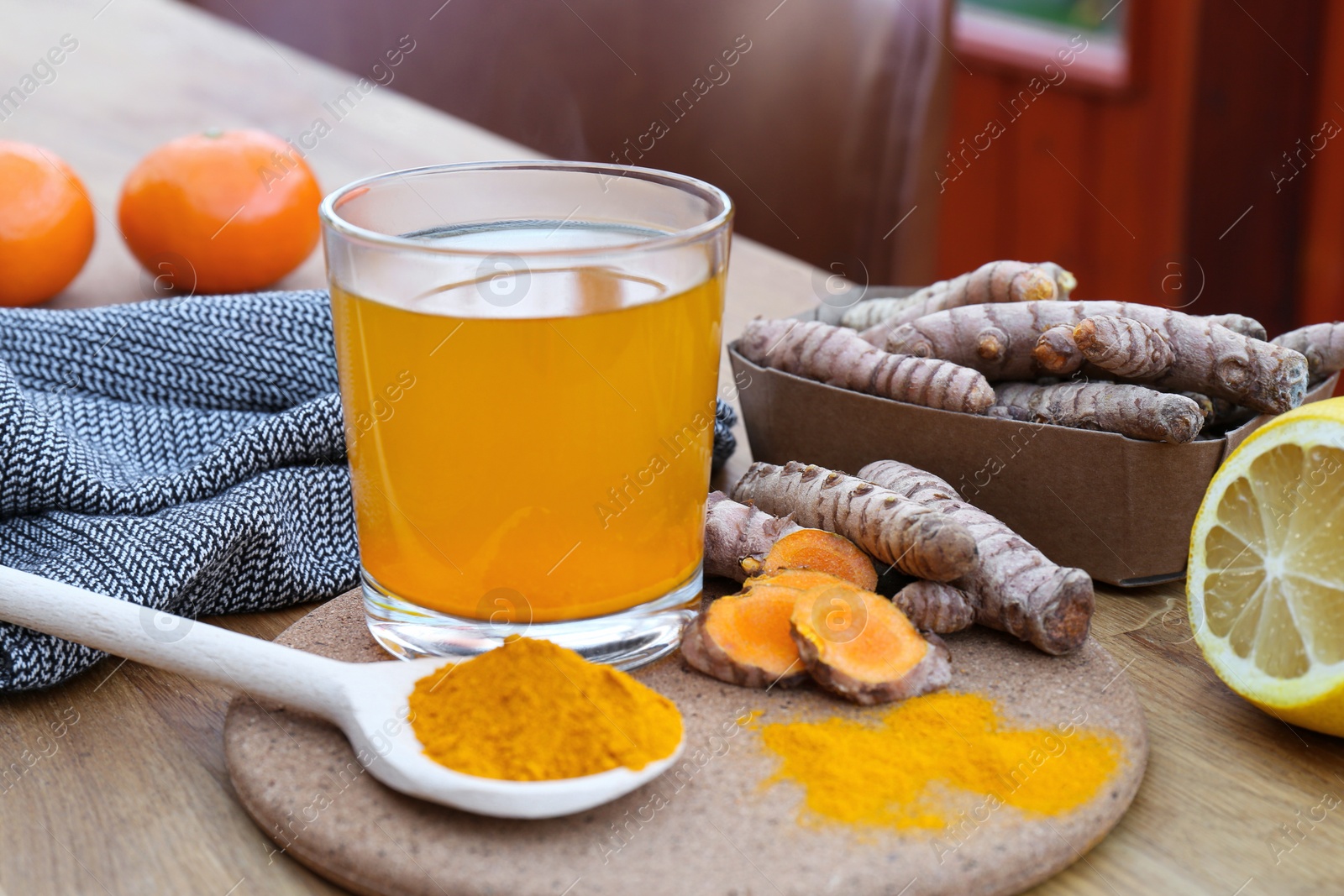 Photo of Glass cup of hot tea, lemon, turmeric powder and roots on wooden table