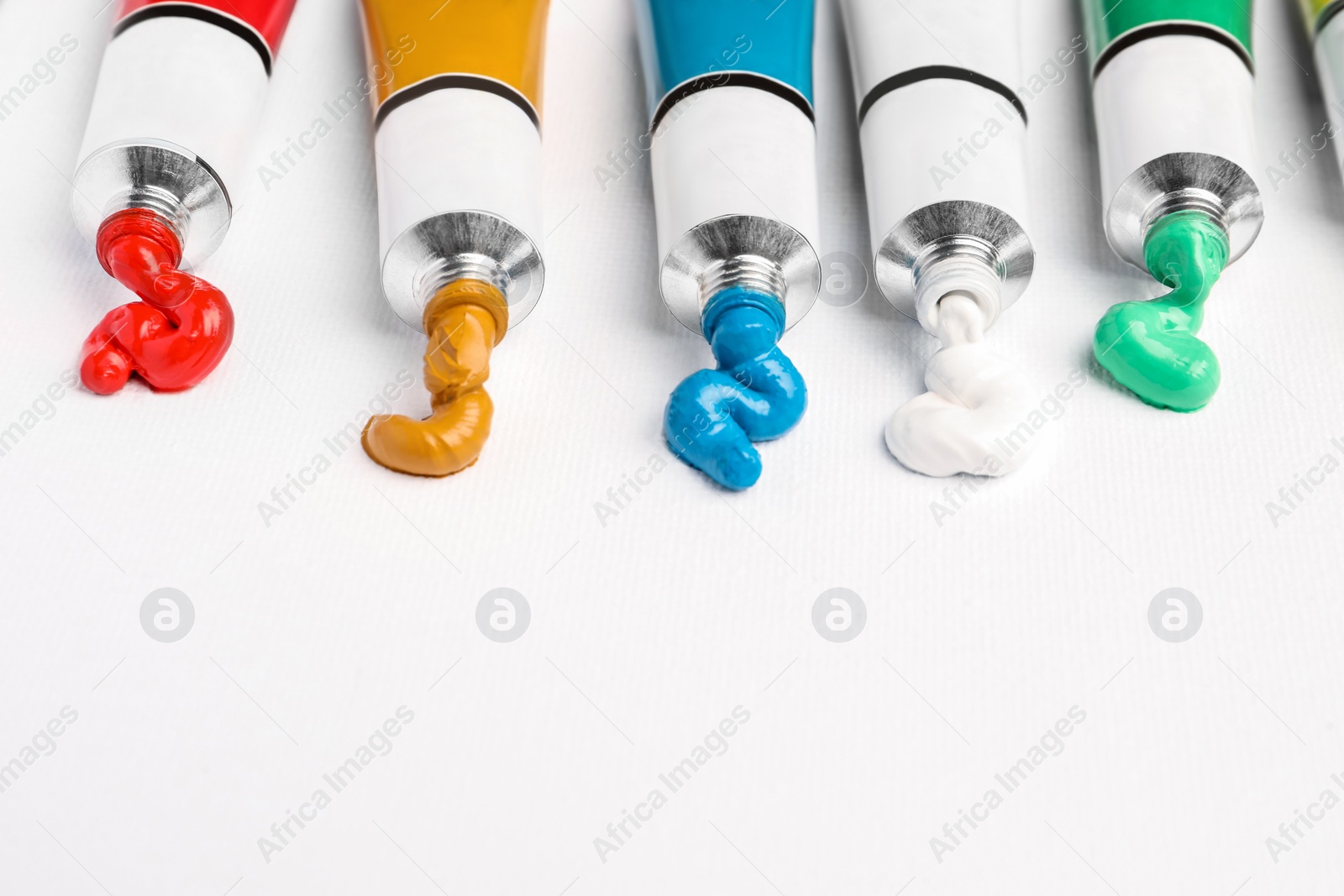 Photo of Tubes with oil paints on white canvas, closeup. Space for text