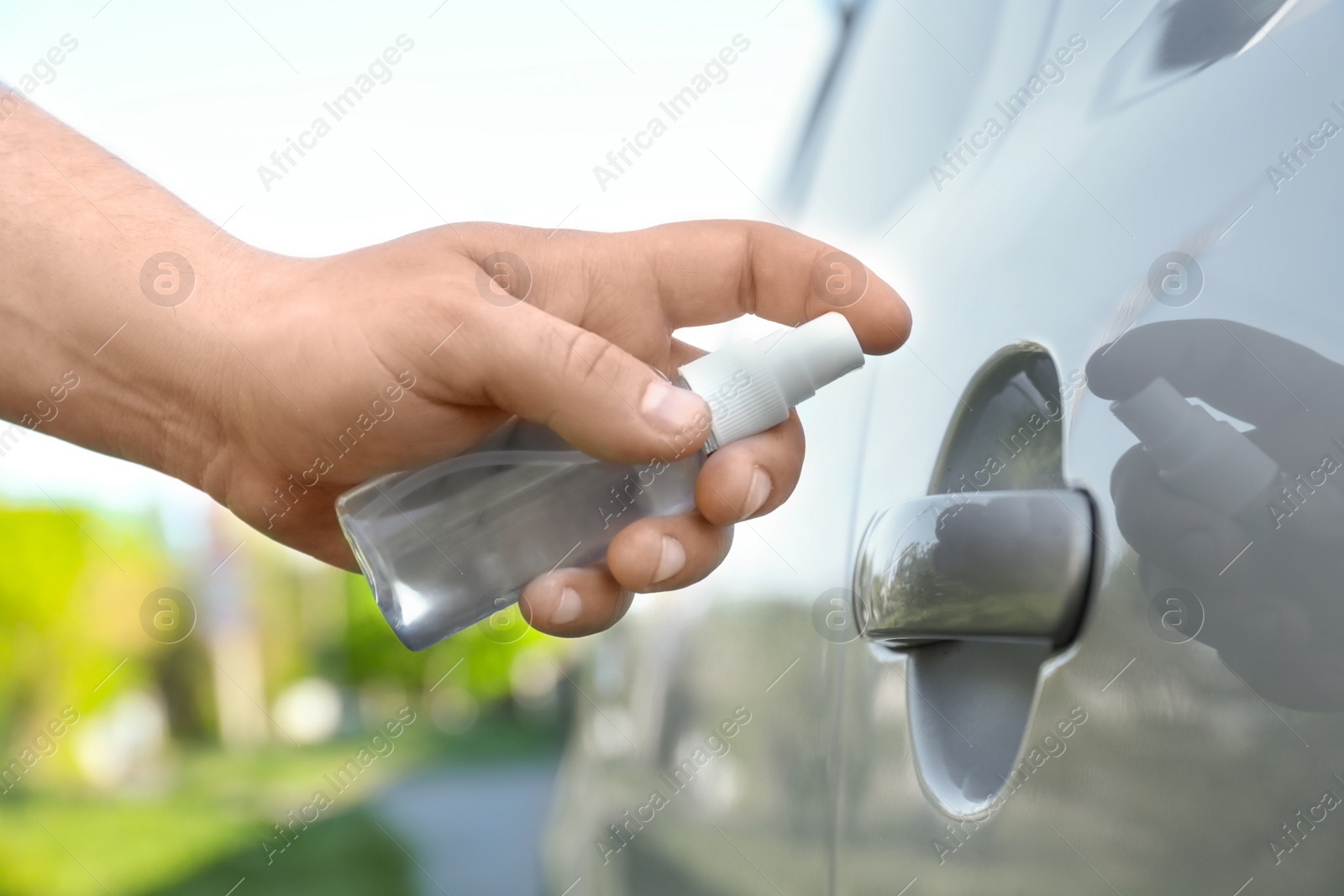 Photo of Man with spray sanitizing car door handle outdoors, closeup