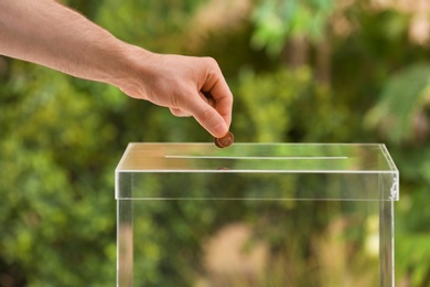 Photo of Man putting coins into donation box on blurred background, closeup