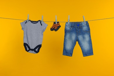 Different baby clothes drying on laundry line against orange background