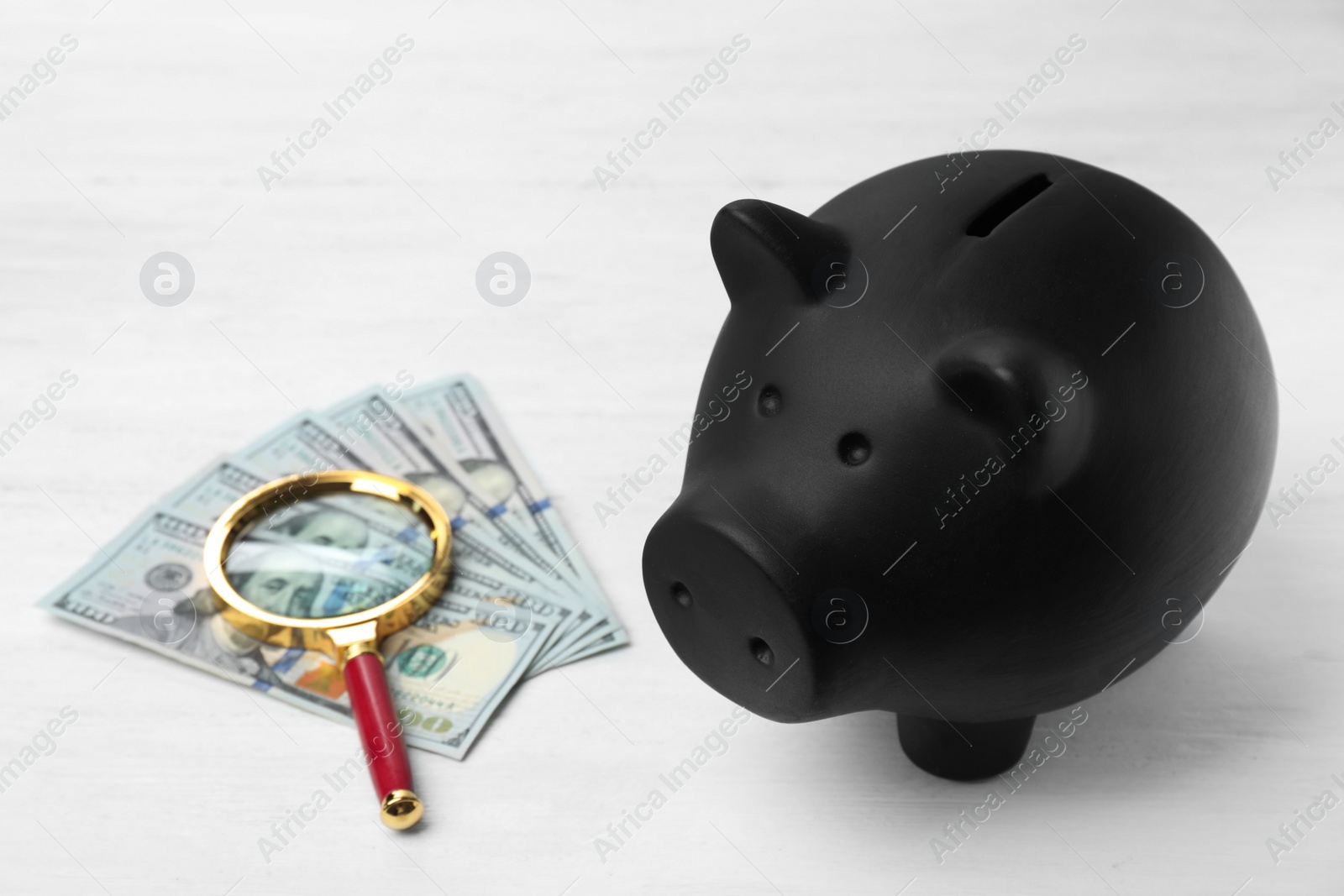 Photo of Black piggy bank, money and magnifying glass on table